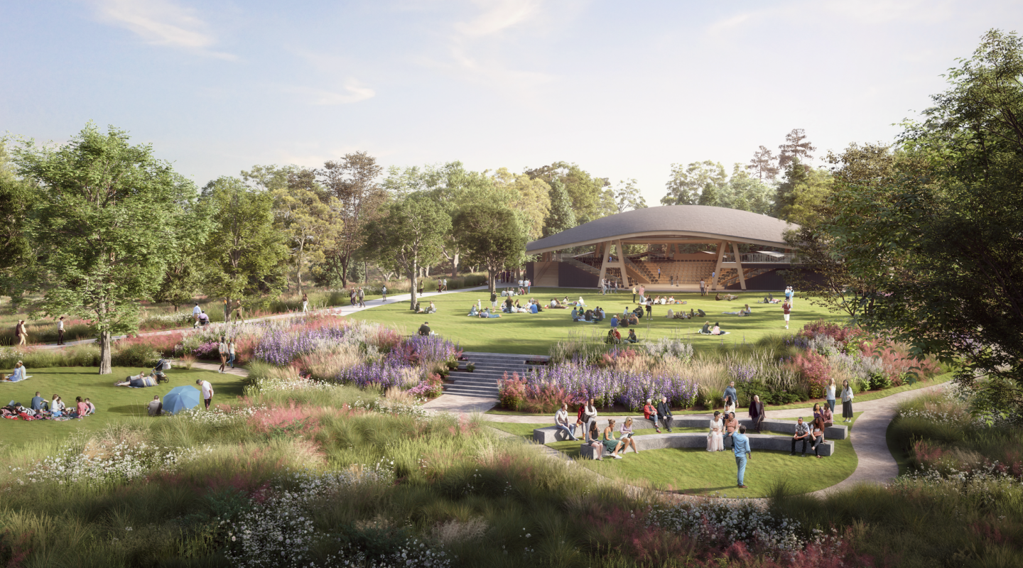 Wide view of the landscape with picnicking patrons scattered across the treed lawn with the open-air theatre behind.